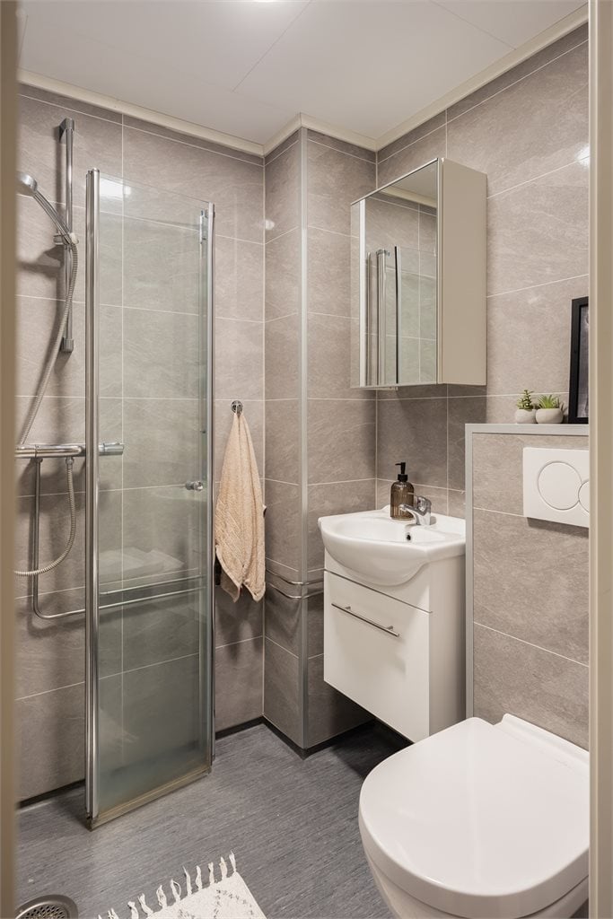 Badet er utstyrt med vegghengt toalett, baderomsinnredning og innfellbare dusjvegger av glass.