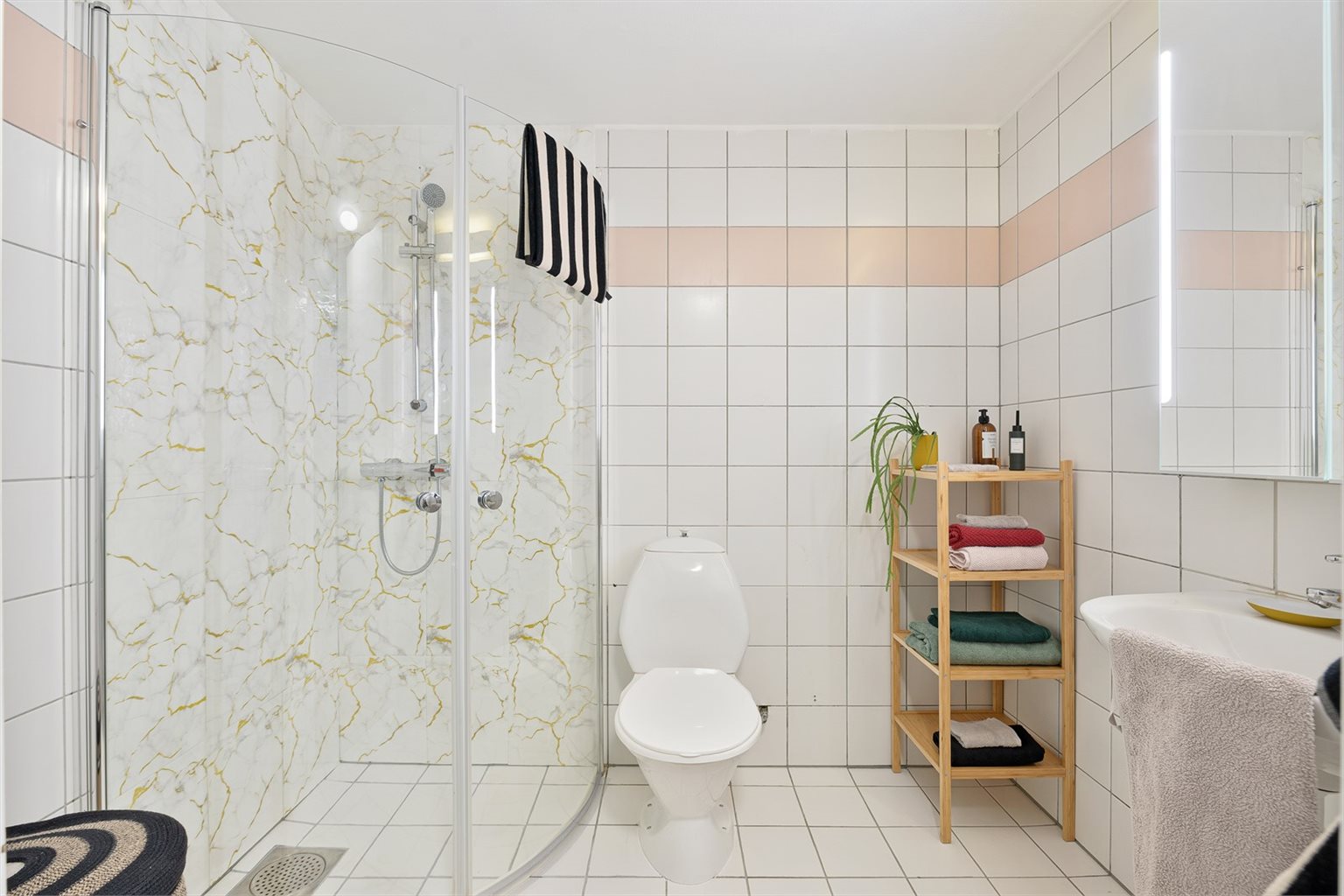 Badet er videre utstyrt med dusjhjørne, mekanisk avtrekk, gulvmontert toalett og servant i skap. 