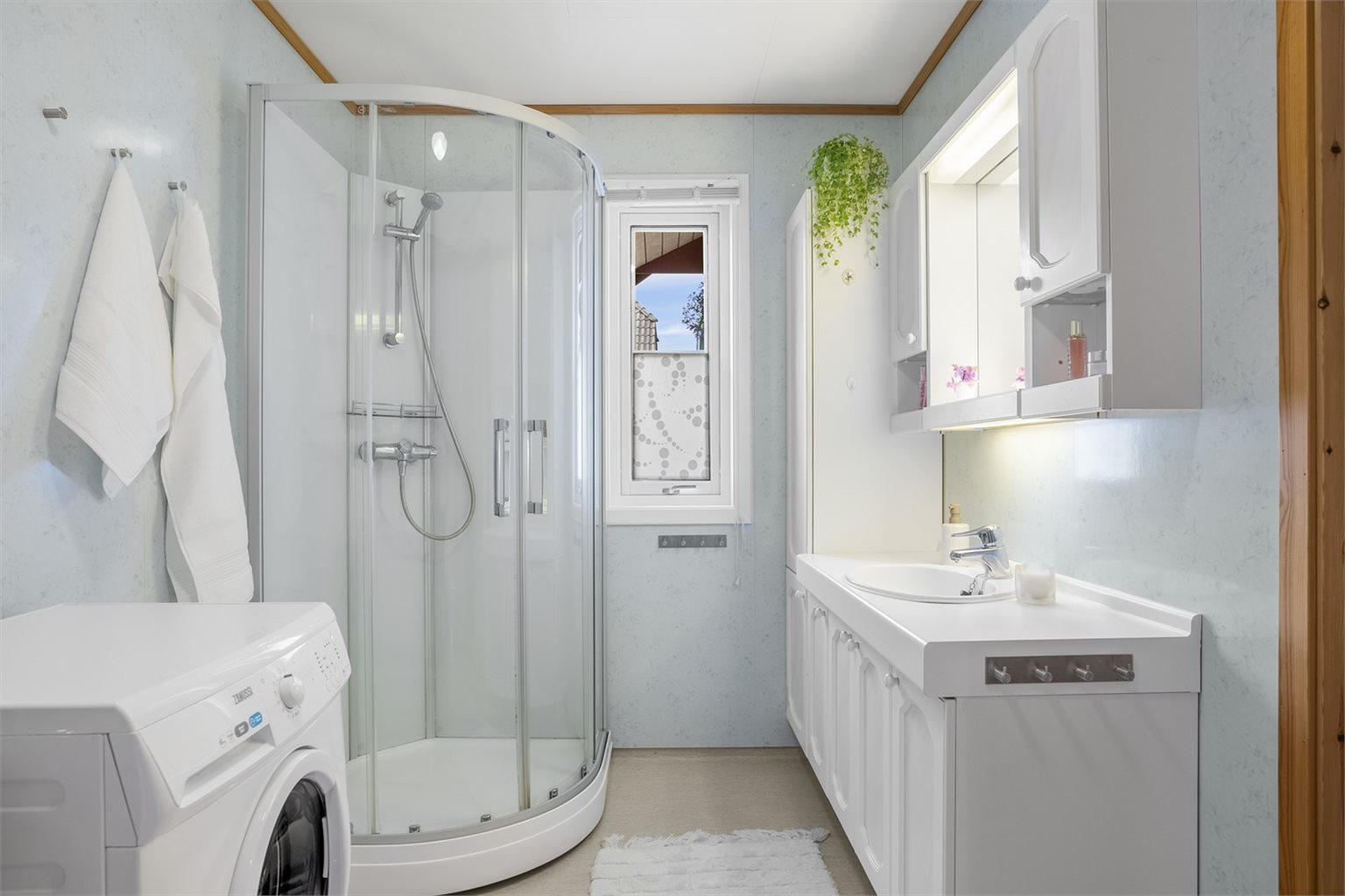 Badet er innredet med stor innredet servant, dusjkabinett, opplegg for vaskemaskin, varmtvannsbereder og utslagsvask.