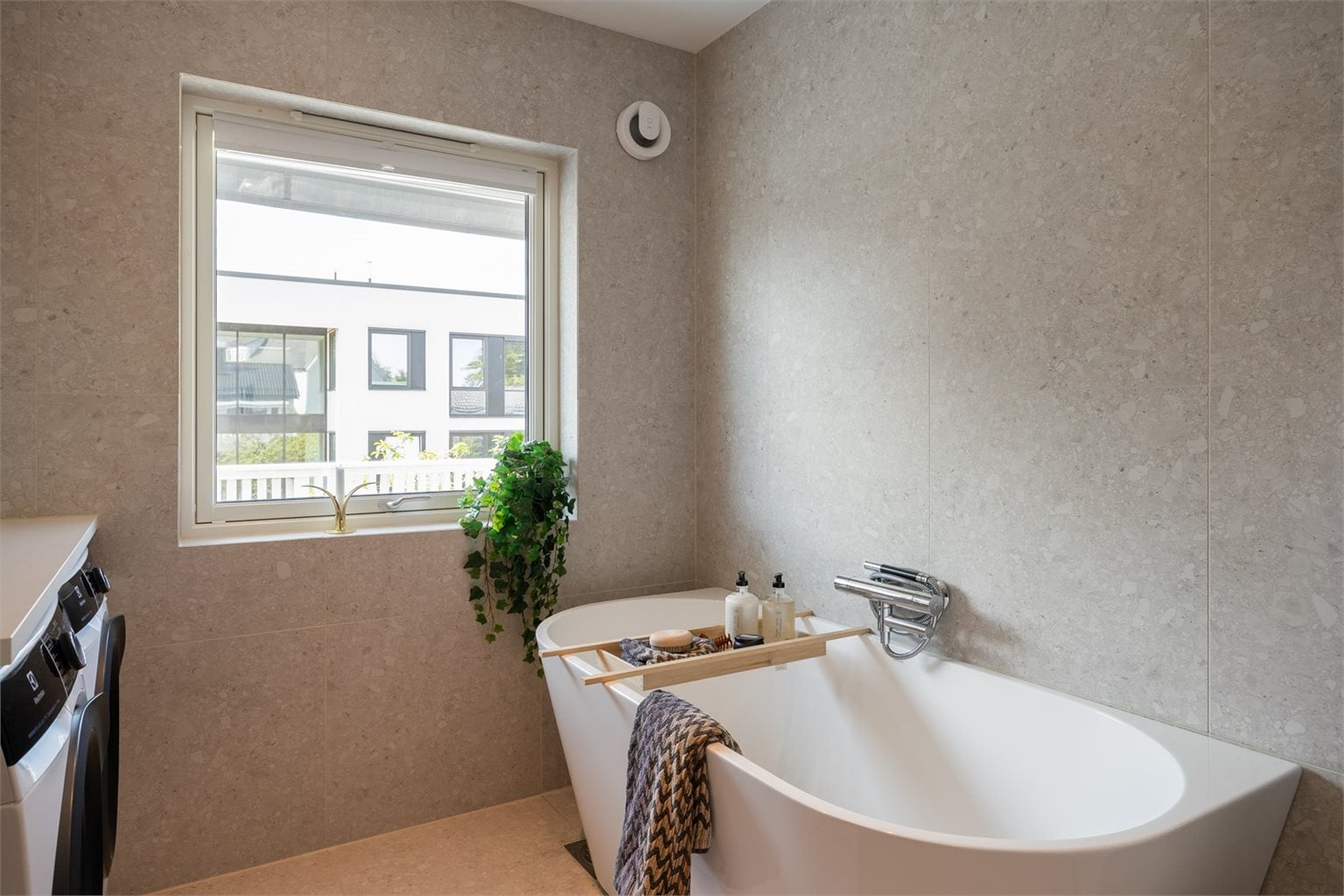 Videre er badet utstyrt med badekar, opplegg for vaskemaskin, mekanisk avtrekk, servant, servantskap og veggmontert wc.