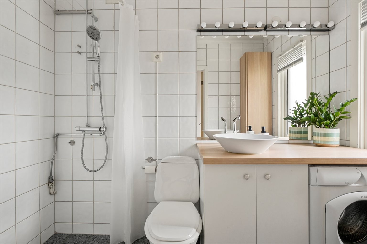Badet er flislagt og utstyrt med dusj, servant med underskap, wc samt vaskemaskin. En arealeffektiv løsning på 3,4 kvm.