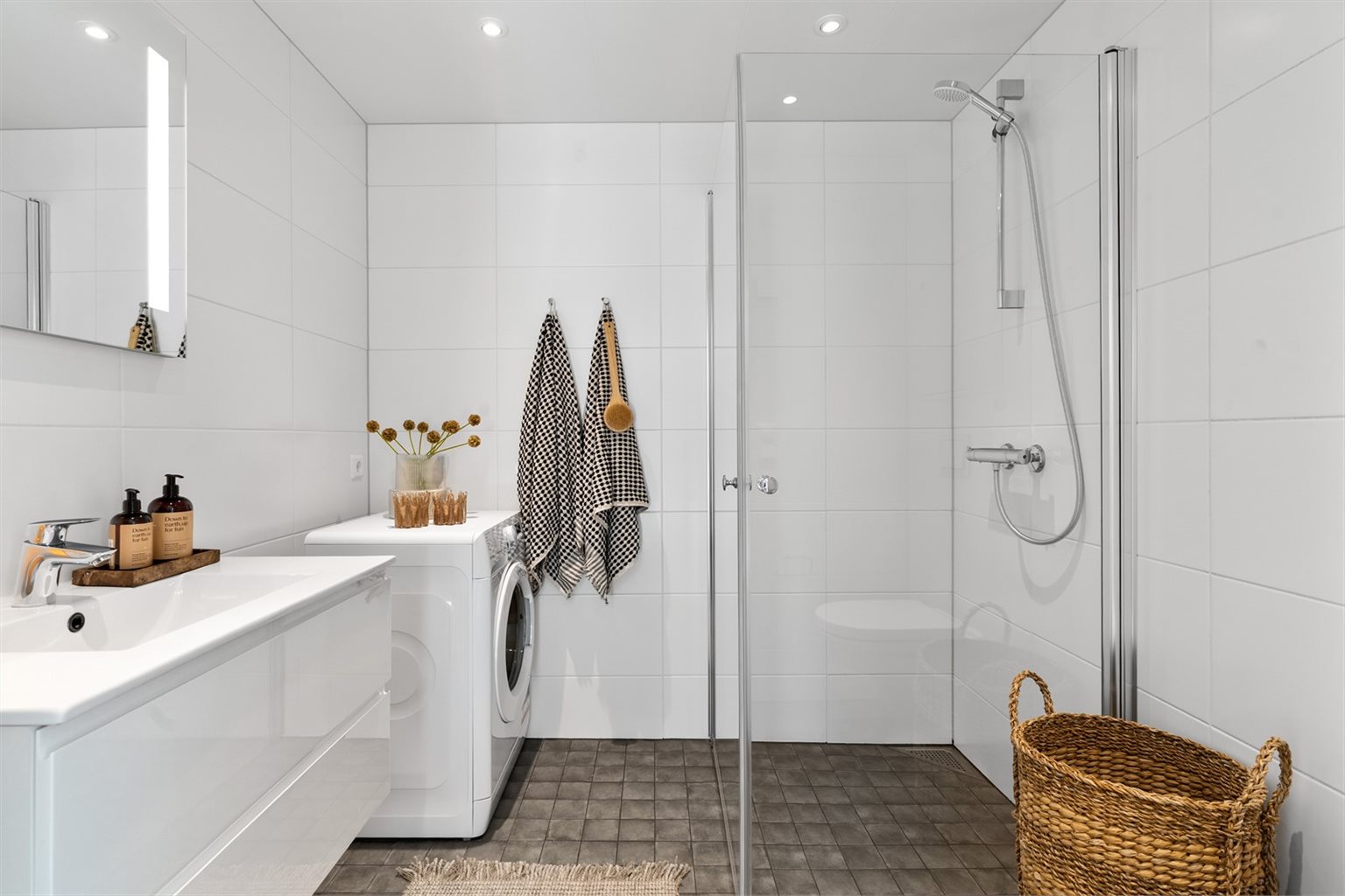 Badet byr på veggfestet innredet servant, praktiske innfellbare dusjdører, opplegg for vaskemaskin og vegghengt toalett.