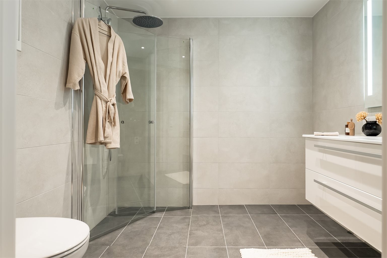 Leiligheten har 2 baderom. Ved soverom 2 finner du et lekkert baderom med innsvingbare dusjdører og regndusj fra Grohe. 