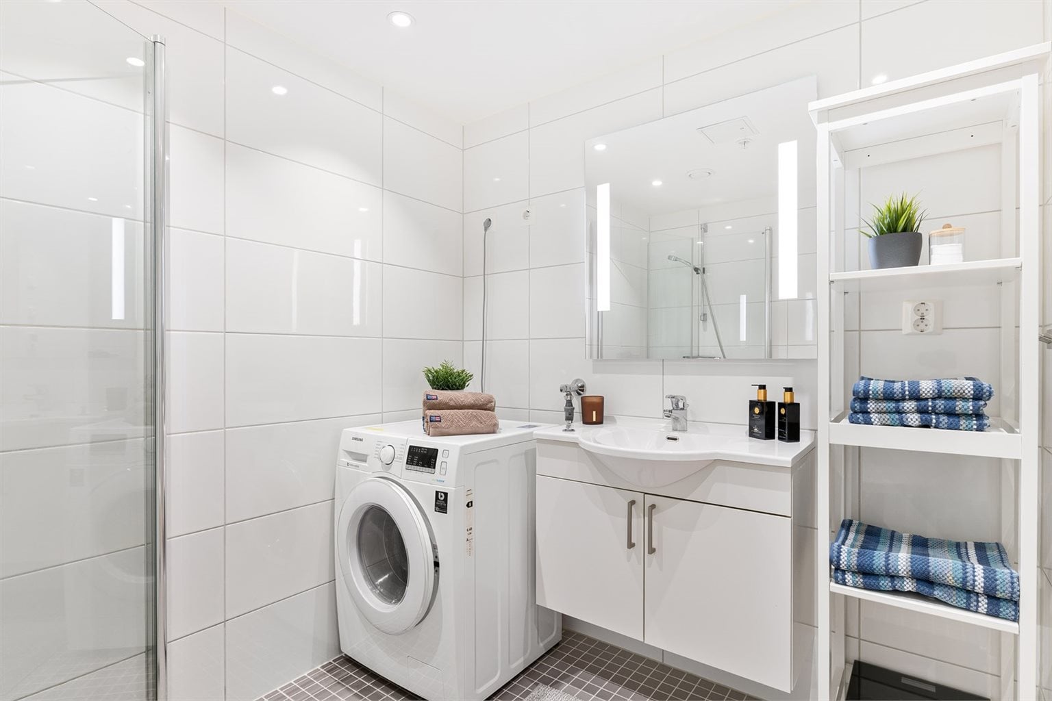 Badet er utstyrt med innfellbare dusjdører, mekanisk avtrekk, toalett, servant i skap, og opplegg for vaskemaskin/tørketrommel. 